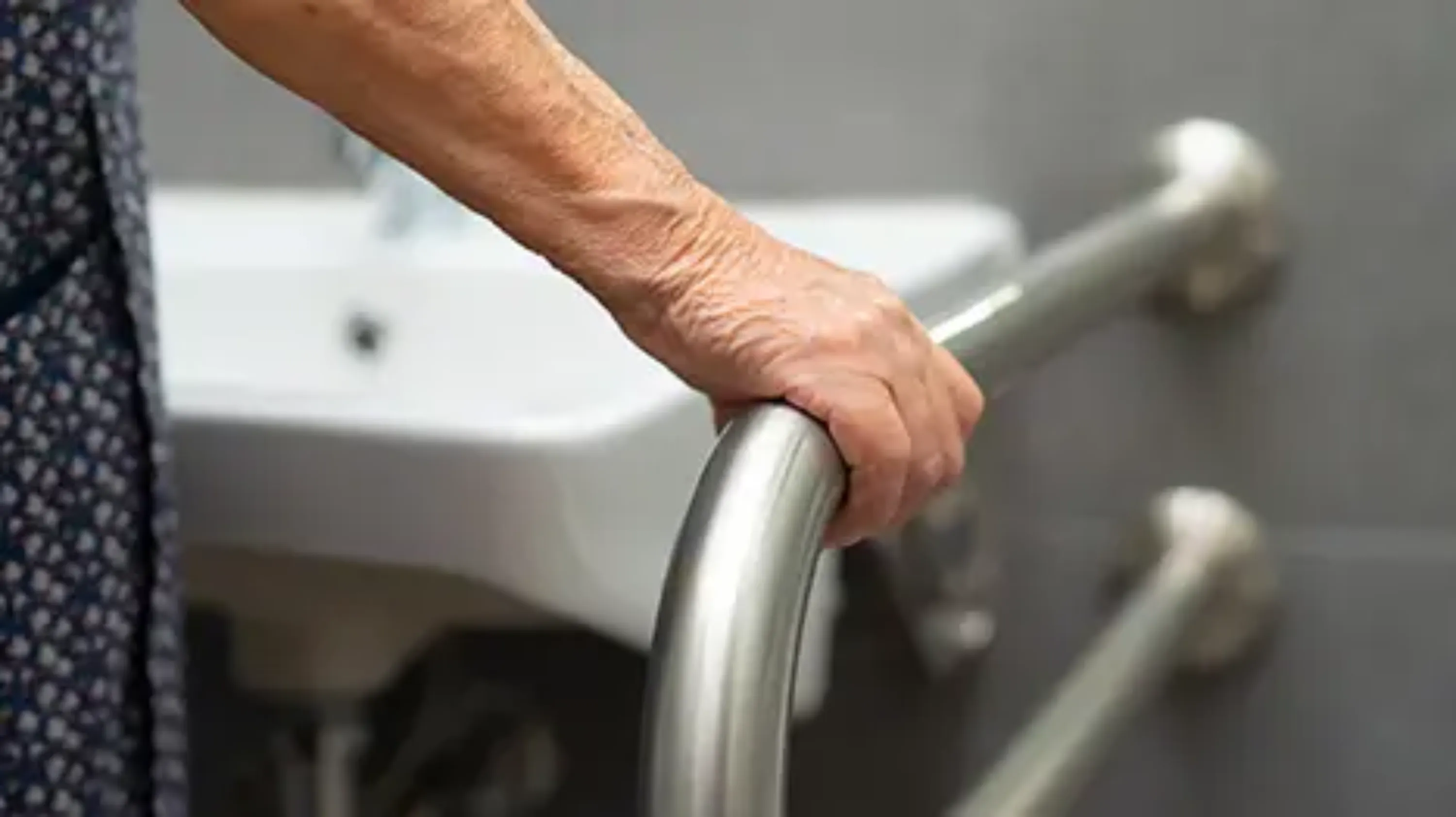 Une personne attrape une barre de soutien à côté d'un lavabo pour se maintenir en équilibre