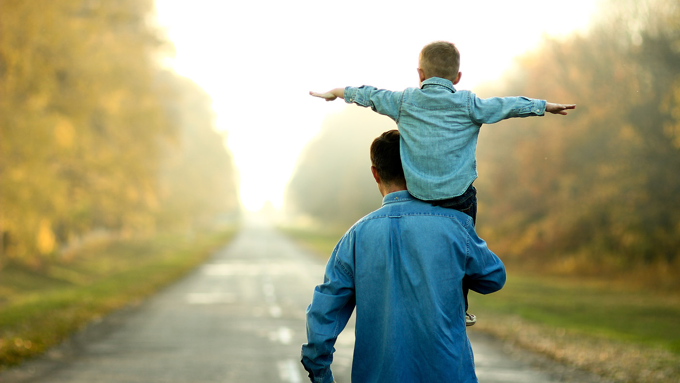Un père porte son fils sur les épaules et ils se tiennent tous les deux sur un chemin de gravier