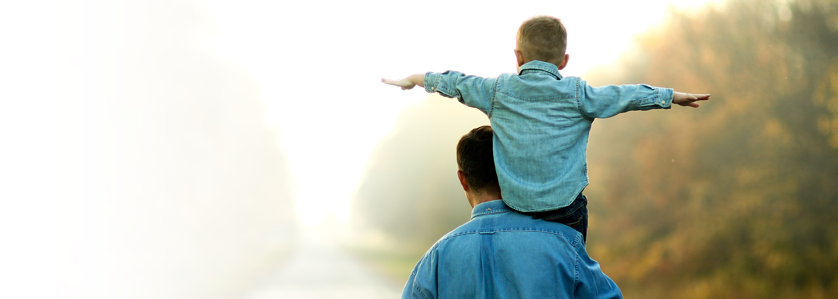 Un père porte son fils sur ses épaules et ils se tiennent tous les deux sur un chemin de gravier