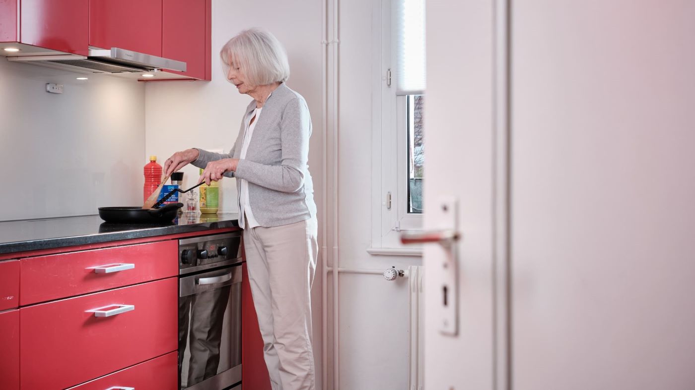 Une femme âgée se tient dans la cuisine et fait la cuisine.