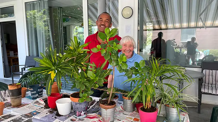 Une dame âgée avec une personne en train de rempoter des plantes